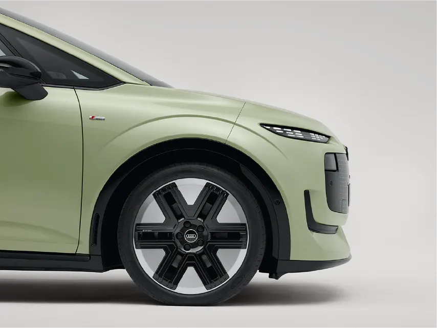 Seitenansicht des vorderen Teils eines hellgrünen Audi mit auffälligen, schwarz-silbernen Alufelgen, schlanken Scheinwerfern und S-line-Emblem vor weißem Hintergrund.