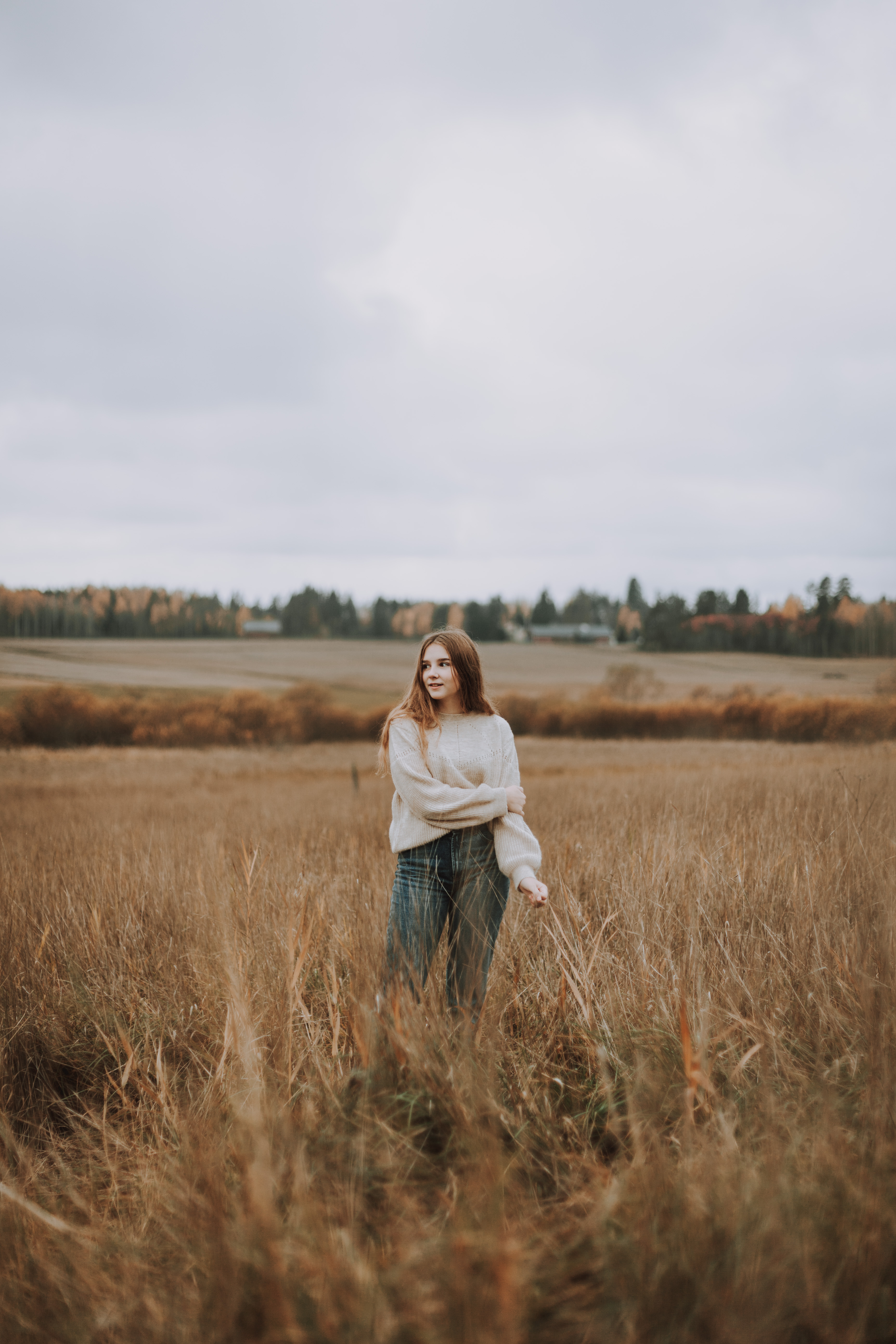 Tyttö seisoo potrettikuvauksessa pellolla valkoinen villapaita yllä