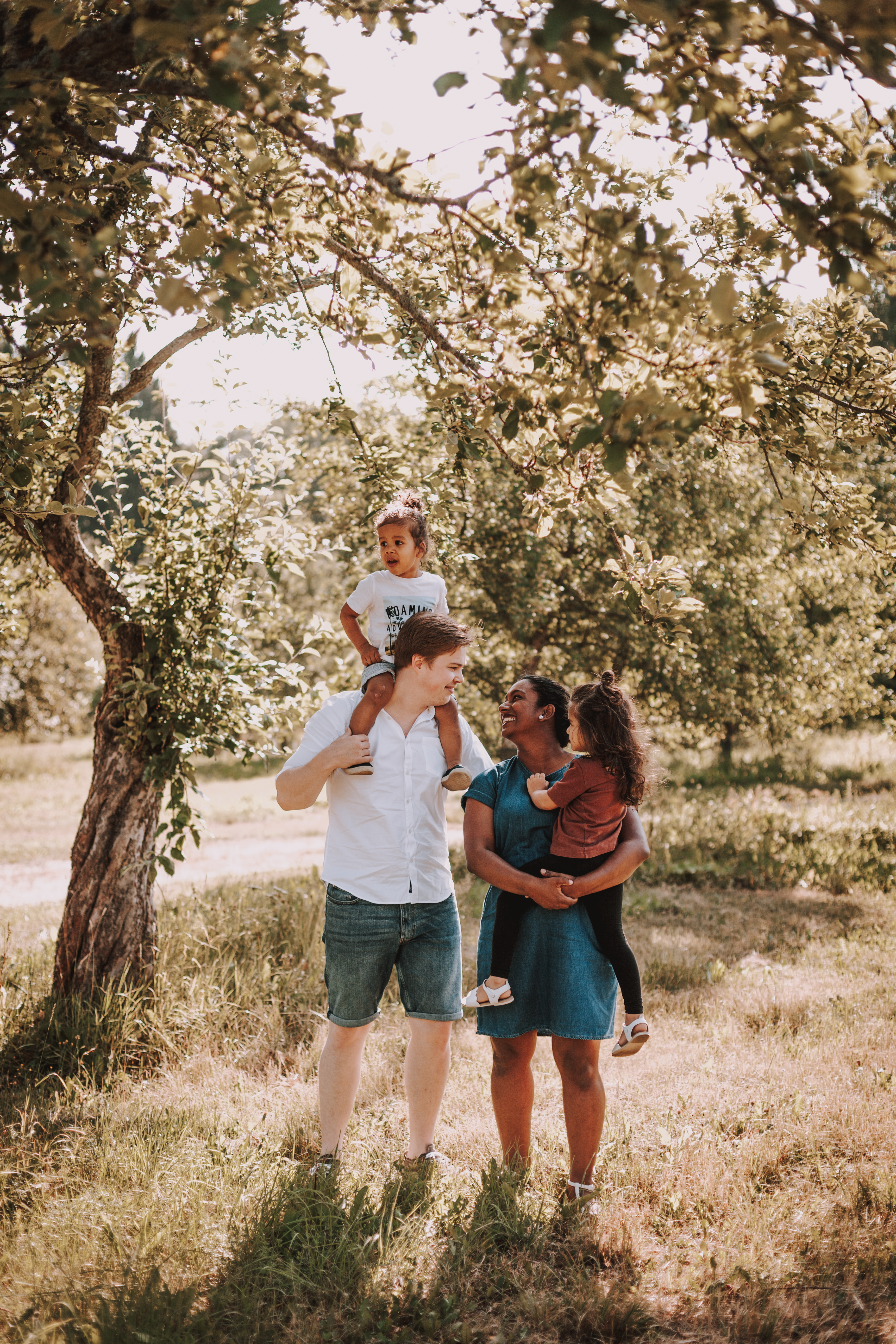 Perhe seisoo omenapuun alla kesän perhepotrettikuvauksessa Malminkartanon omenatarhassa Helsingissä