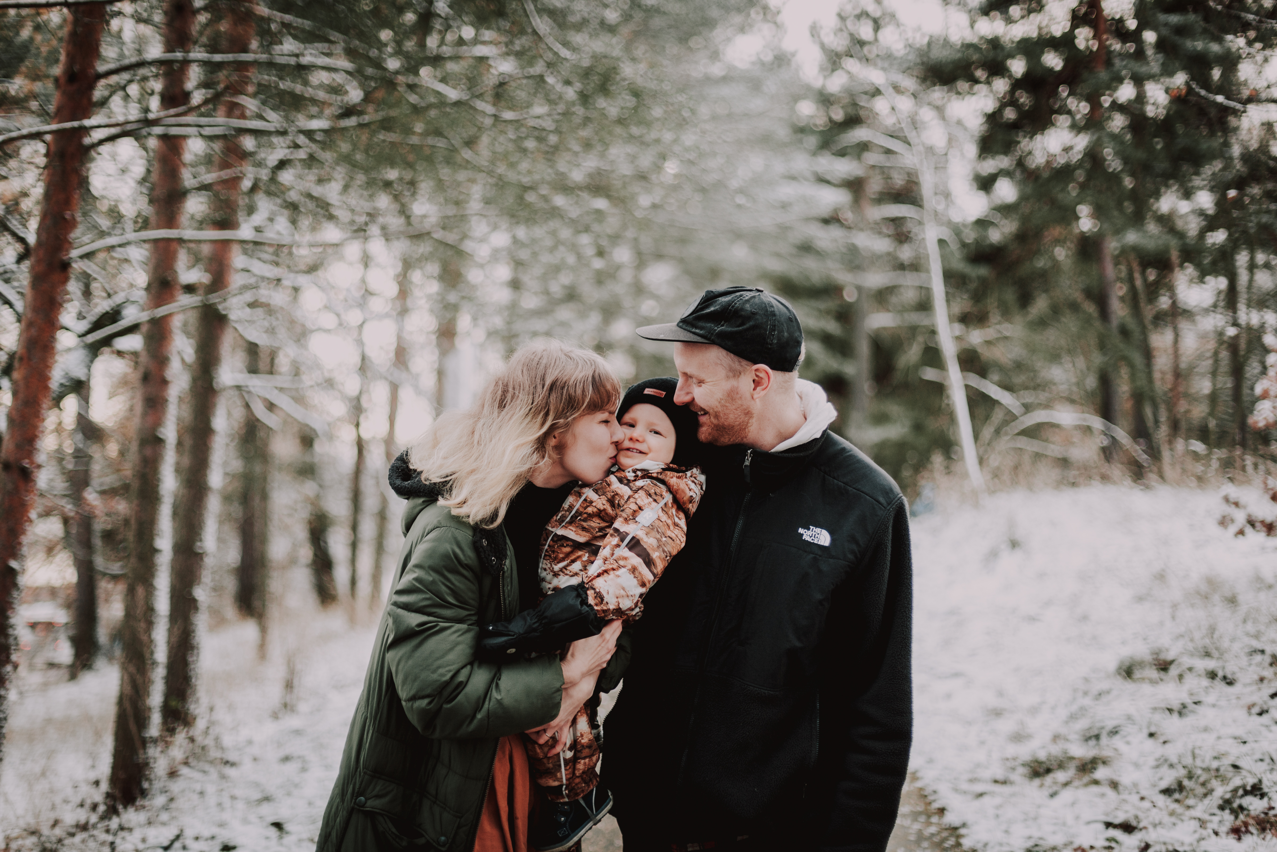 Talvi-perhekuvaus miljöössä Helsingissä. Vanhemmat ja 1-vuotias nauravat.