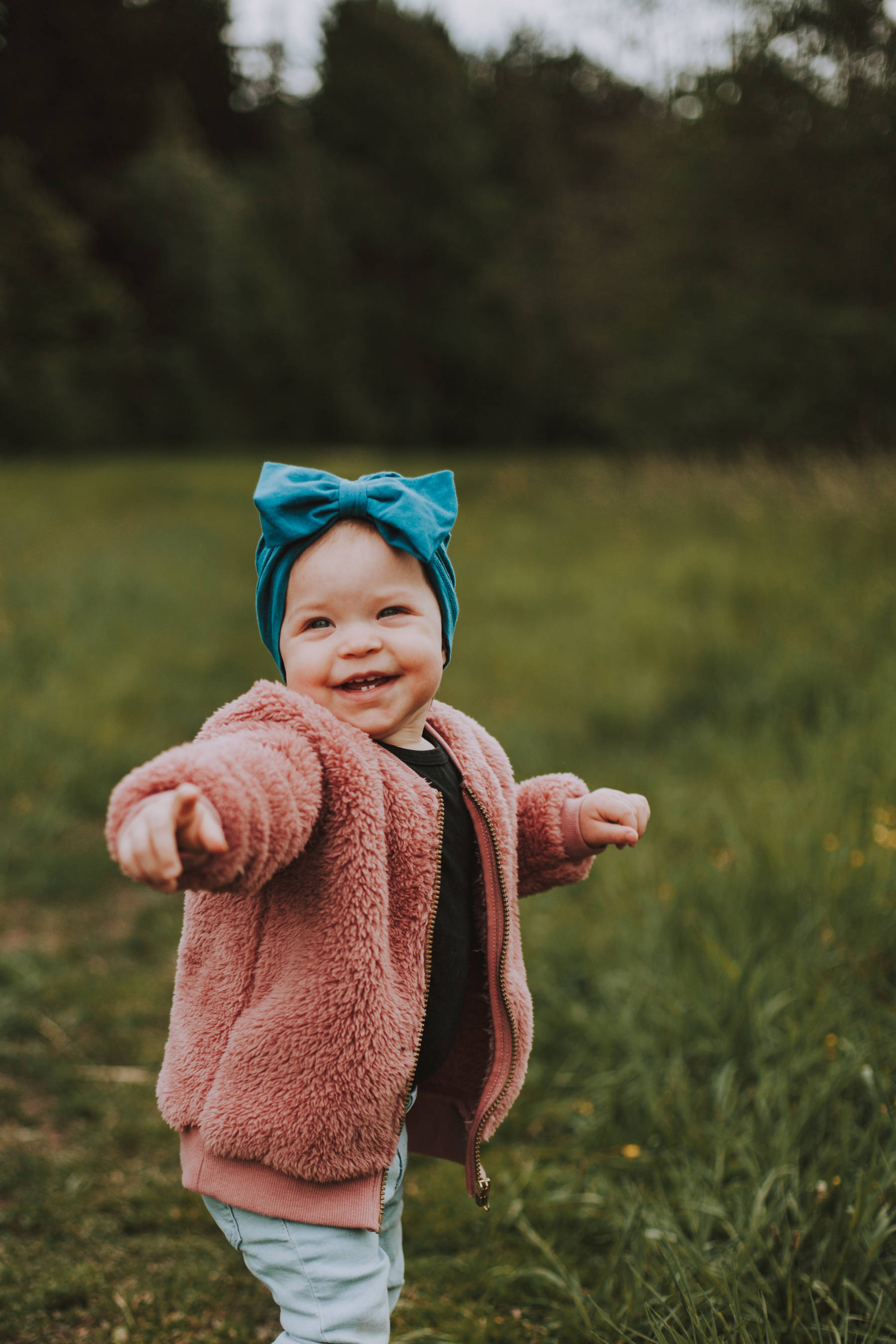 Naurava lapsi sinisella hiuspannalla seisomassa pellolla perhekuvauksessa