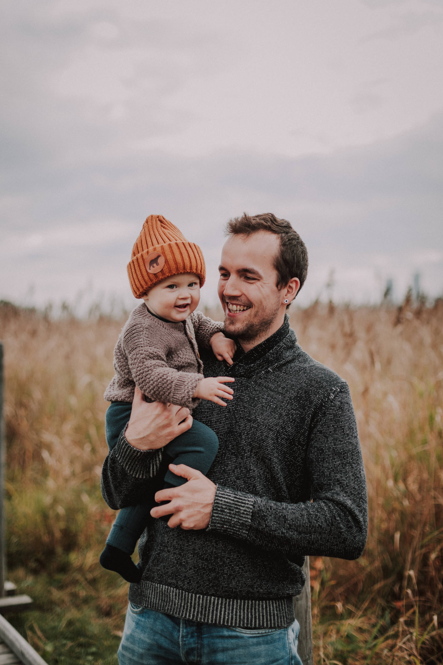 Isä ja poikavauva nauraa perhekuvauksen aikana Lammassaaressa Helsingissä villapaidat päällä