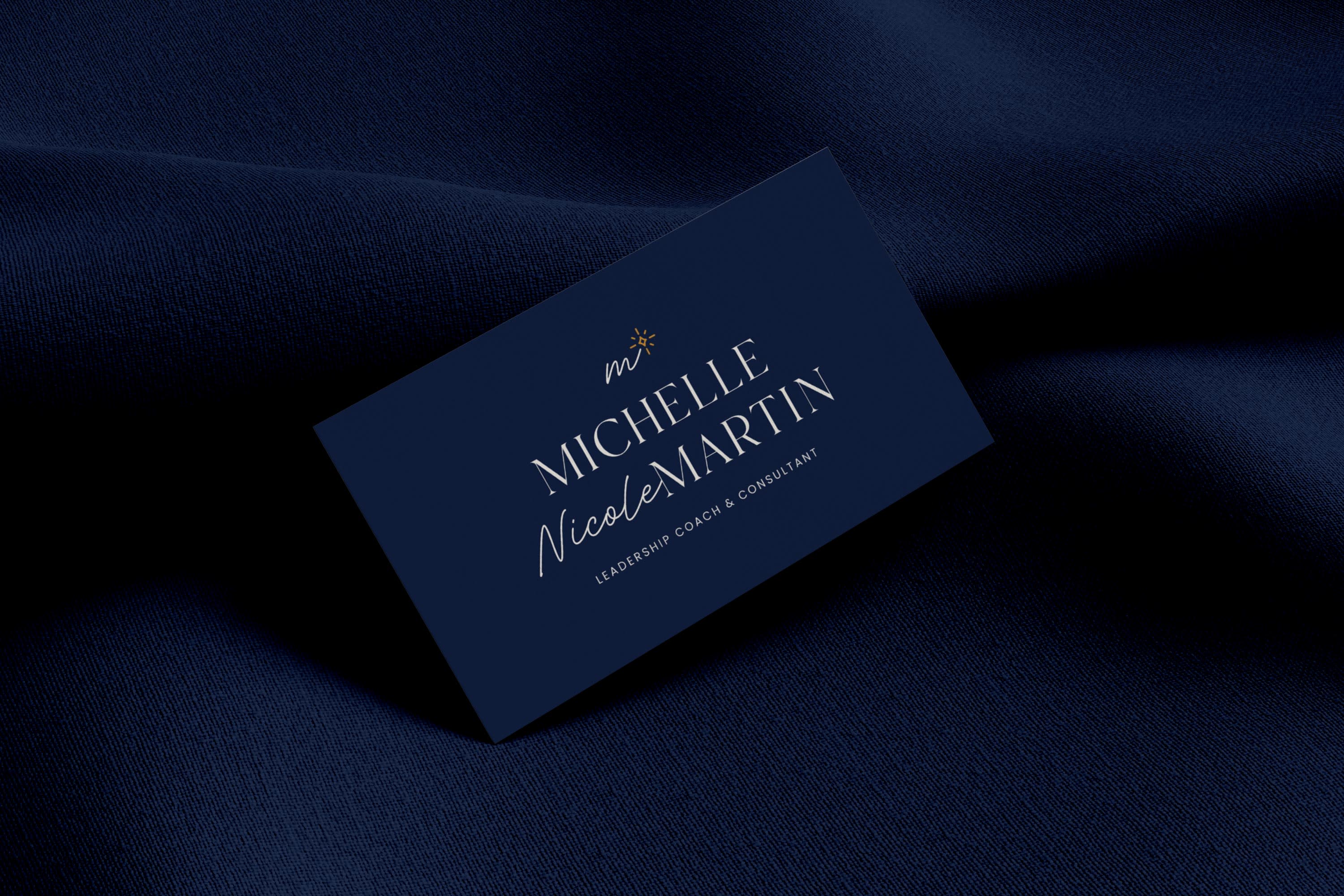 A deep blue business card is shown displaying the custom logo design for Michelle Nicole Martin.