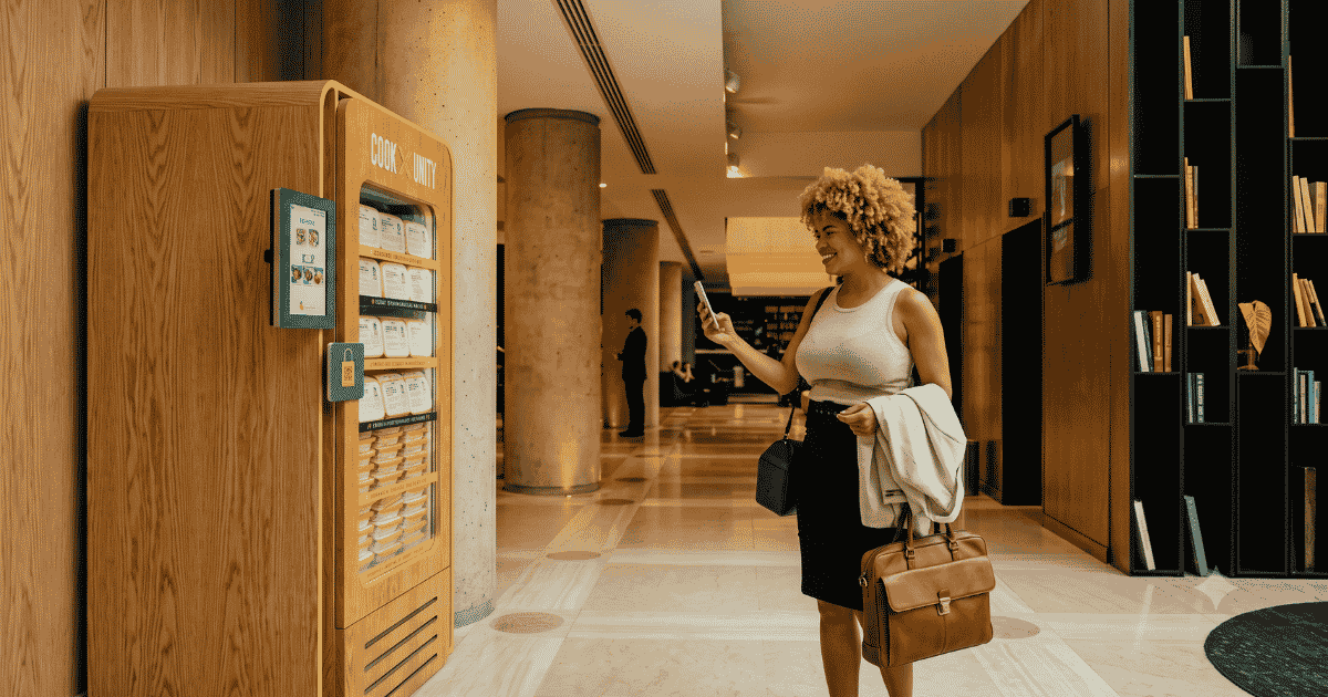 Resident using a smartphone to select a meal from a CookUnity smart fridge in a luxury apartment building lobby