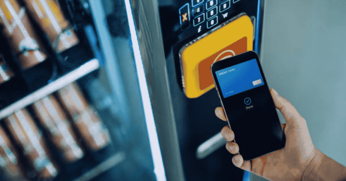 Person using a smartphone to make a contactless payment at a traditional vending machine