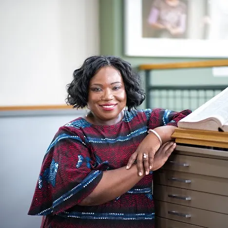 A Black woman with short, wavy hair poses next to archives