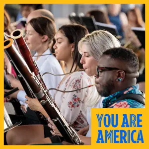 A musician in a bright suit sits holding a trombone, capturing a close-up moment before a performance.