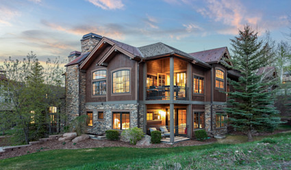 Exterior of Alpine Ridge home with a mix of wood siding and rock with two covered patios all shot during dusk. 