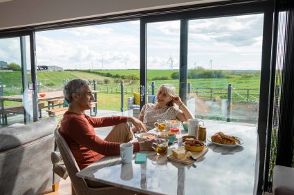 A couple has brunch near the open doors to their patio while discussing how happy they are after buying a second home.