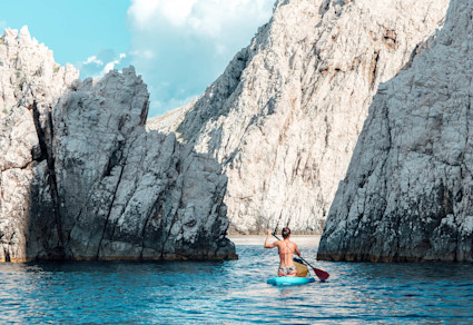 A nature-lover in a blue kayak paddles around rocks, a fun thing to do in Cabo.