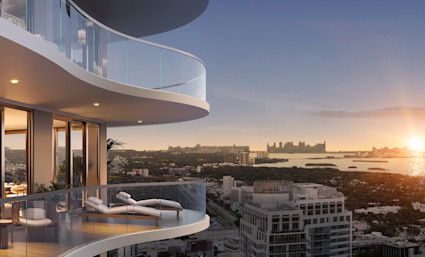 Curved glass balcony with chaise loungers overlooking Miami's skyline and bay at golden hour.