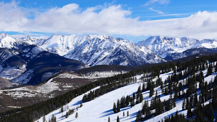 Snow-covered mountains with pine trees and ski slopes capture the winter beauty, often compared in Vail vs. Aspen resorts. 