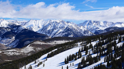 Snow-covered mountains with pine trees and ski slopes capture the winter beauty, often compared in Vail vs. Aspen resorts. 