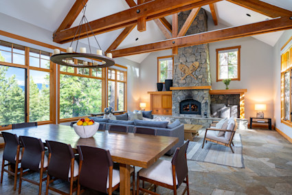 A spacious dining room with a high, vaulted wood-beamed ceiling and a stone fireplace.