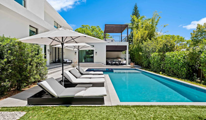 Casa Estrada pool area with pool and hot tub and poolside lounge chairs with umbrellas and a small covered area with a grill station. 