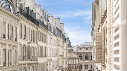A classic Parisian street scene with elegant, historic buildings and a distant glimpse of the Eiffel Tower, representing the timeless beauty and architectural grandeur found in luxury vacation destinations.