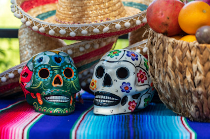 Sugar skulls resting on a colorful table with a basket of fruit.