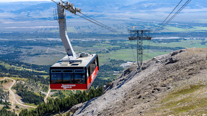 A red and black cable car ascends the snowy mountains of Jackson Hole, offering a panoramic view of the valley and highlighting the region’s iconic winter adventure appeal. This dynamic scene encapsulates the excitement of catching the first runs of the season in a world-class ski destination.