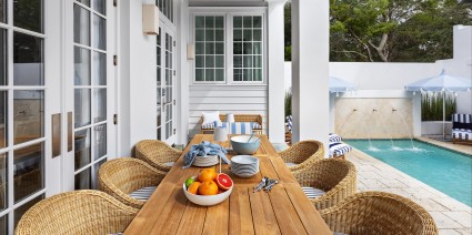 A outdoor table at a Florida 30A vacation home with wicker chairs and a bowl of fruit on it.
