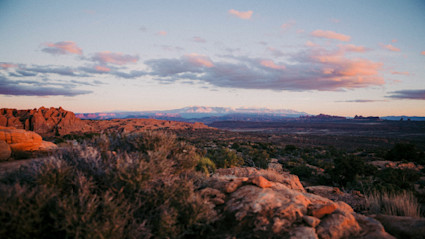 This captivating sunset scene over the Scottsdale desert features dramatic red rock formations and snow-capped mountains under a pastel sky, perfectly capturing the peaceful and inspiring mood of a fall escape in the Southwest.
