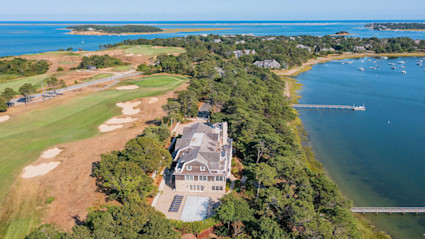 A striking aerial view of a luxury Cape Cod property adjacent to a golf course, with private dock and boats on the water, exemplifying the allure and investment potential of coastal real estate in the evolving Cape Cod market.