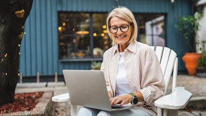 Happy woman using a laptop outside a modern building, planning her next trip on one of the best vacation rental sites.
