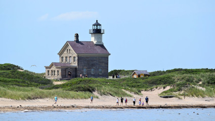 Families walk along the beach near a lighthouse on Block Island, a great activity for pet-friendly vacations.