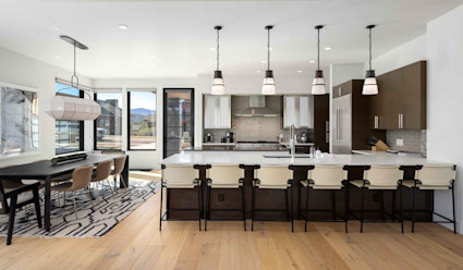 Kitchen area with dining table that seats eight and kitchen with land island with stools pulled up and stainless steel appliances. 