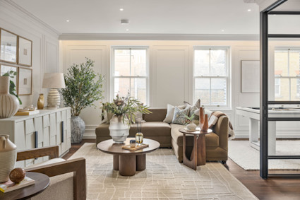 Warm, layered living room with paneled walls, natural wood accents, and steel-framed glass doors opening to a sunlit adjoining space.