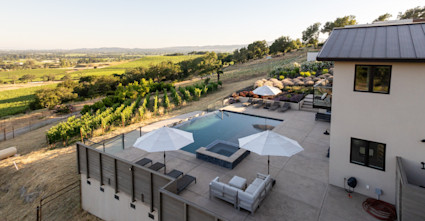 Rear exterior and view of Loma Vista with the pool and hot tub with poolside lounge area and vineyard view.