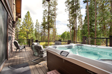 A private hot tub on a wooden deck of a Breckenridge vacation home, overlooking snow-covered trees, perfect for apres-ski relaxation.