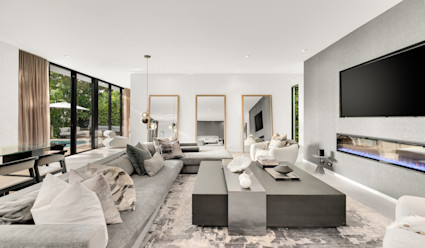 Venetian living room with a long grey chaise sectional facing a wall-mounted flat screen tv with multiple full length mirror and floor to ceiling windows that look out to the pool area.