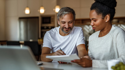 Two people calculate their down payment using a laptop, pen and paper.
