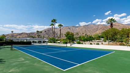 A vibrant Palm Springs tennis court with palm trees and mountains in the background, capturing the active lifestyle and desert landscape perfect for pickleball enthusiasts.