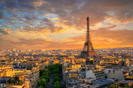 A breathtaking landscape view of the Eiffel Tower at sunset in Paris, with classic Parisian rooftops in the foreground and the city bathed in warm golden hues. This iconic, emotionally resonant image captures the allure of global luxury travel and aspirational living.