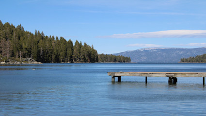A tranquil autumn scene at Lake Tahoe with a wooden pier and forested shoreline, embodying the peaceful atmosphere ideal for bird watching.
