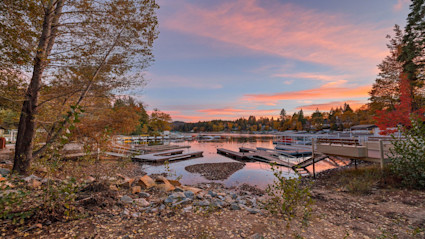 Serene lakeside sunset at Lake Arrowhead, CA with docks and colorful autumn foliage, perfectly capturing the tranquility and natural beauty associated with luxury alpine lakefront living.
