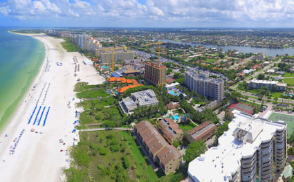 Aerial view of Marco Island, FL, featuring white sand beaches, Gulf waters, beachfront hotels, condos, and inland waterways under blue skies.