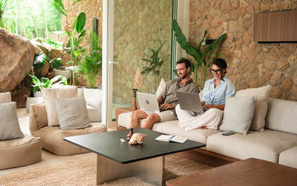 Two people use their computers in their luxury vacation homes.