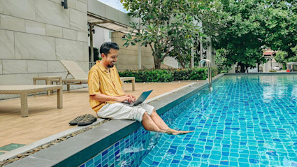 A person researches Plum Guide alternatives on their laptop while sitting by a pool.