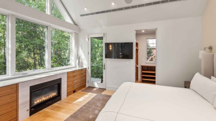 A tastefully decorated bedroom featuring a cozy fireplace, television and woodland views.