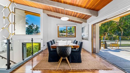 An elegant vacation home dining room with beamed ceilings and a large sliding door that opens to a spacious deck