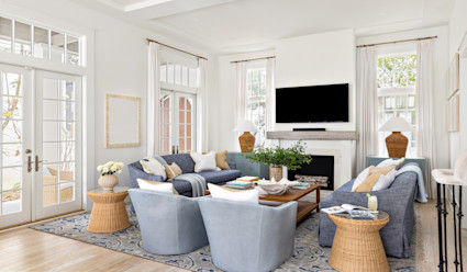 Living area with blue-colored furniture arranged around a coffee table in front of a fireplace with a wall-mounted flat screen tv hanging above.
