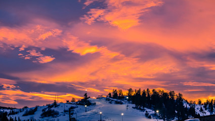 A stunning sunset over the snowy mountains of Steamboat Springs, CO, with vibrant hues of orange, pink, and purple illuminating the sky. The dramatic colors and serene landscape evoke the ultimate summer sunset experience, making it perfect for capturing the essence of a sunset happy hour at Thunderhead Lodge.