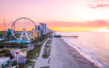 People play in the water in front of a large Ferris wheel in North Myrtle Beach, one of the best spring break ideas for families.