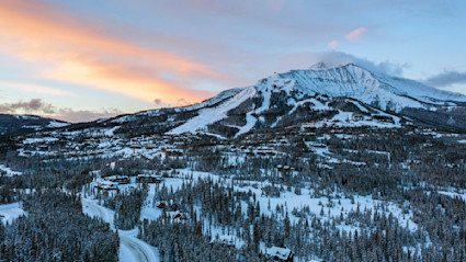 Aerial view of the snow-capped mountain range and trees at sunrise.