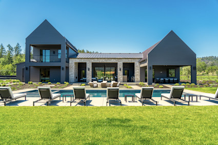 Exterior view of the Bennett pool area featuring a vibrant, manicured lawn, poolside lounge chairs, and a full view of the home’s floor-to-ceiling windows.