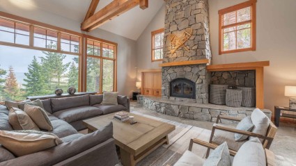 A great room of a Truckee second home with a beamed ceiling, stone fireplace, modern furniture and stone floors