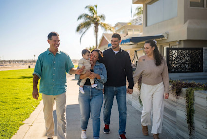 Family walking hand-in-hand down a paves sidewalk with one woman holding a infant child.