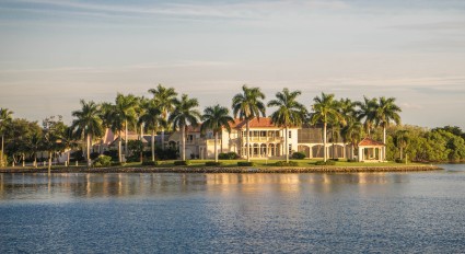 A large, waterfront mansion with several tall palm trees